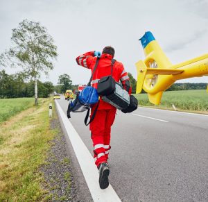 Doctor with defibrillator and other equipment running from helicopter. Teams of the Emergency medical service are responding to an traffic accident.