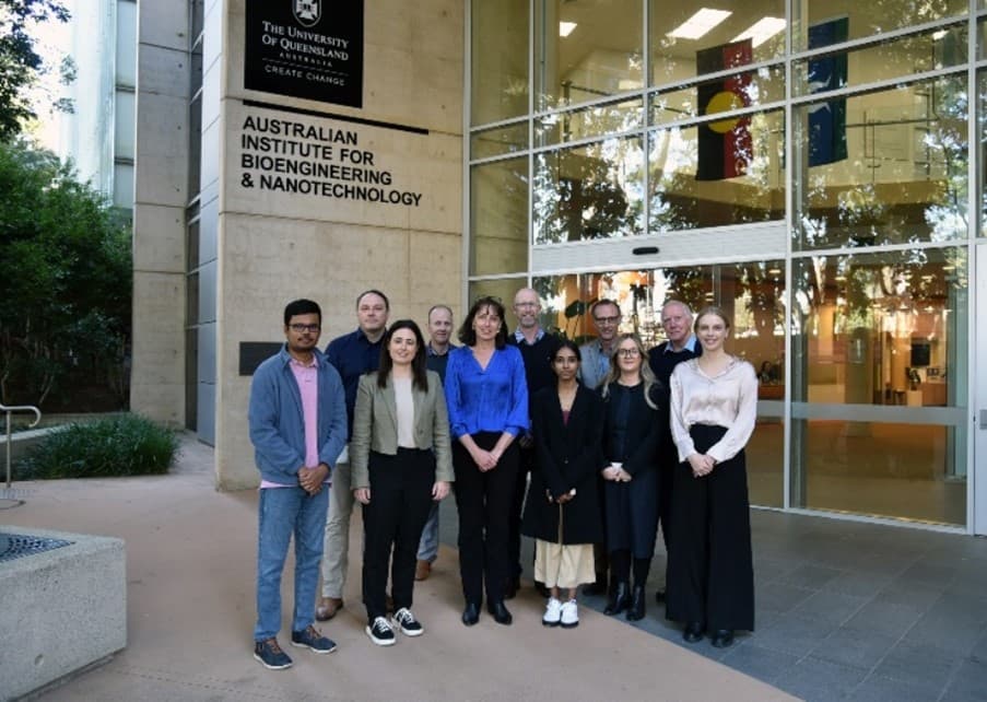 Eleven people stand in front of the glass and concrete front doors of a building. Above them is a sign that reads: "The University of Queensland" and "Australian Institute for Bioengineering & Nanotechnology."