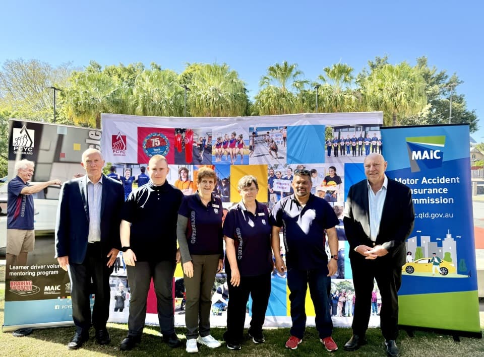 Six people stand in front of banners that read "MAIC" and "PCYC".
