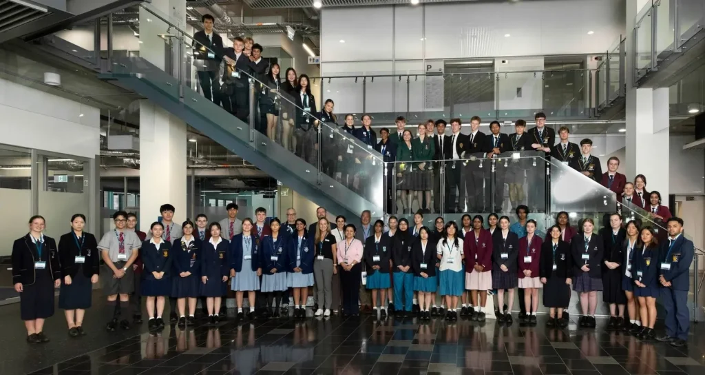 Large group of students (76 students) from various high schools, in school uniforms, standing in front of and on a staircase at QUT.